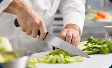 Chef slicing celery with a Victorinox Fibrox chef’s knife on a white cutting board